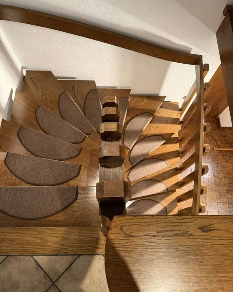 Projekte Perspektive von oben auf die Kurve einer massiven Holztreppe mit braunen Stufenmatten vor der Liftmontage.