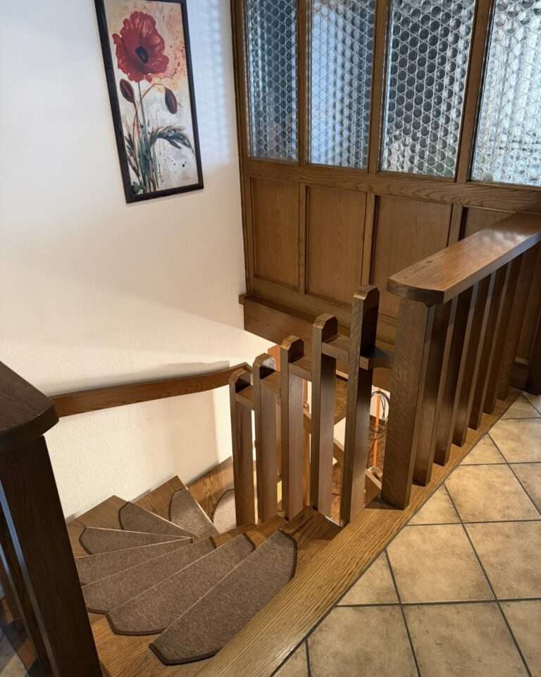 Projekte Gewendelte Holztreppe mit Holzgeländer, auf der ein maßgefertigter Kurven-Treppenlift montiert wird.
