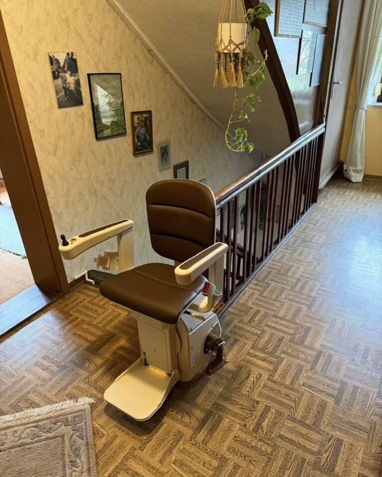 Projekte Der braun gepolsterte Kurventreppenlift von Paitsch Lifte in seiner sicheren Parkposition auf dem Parkettboden der oberen Etage.