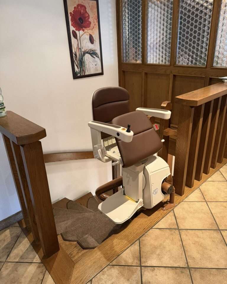 Projekte Der installierte Kurventreppenlift von Paitsch Lifte in der Parkposition am oberen Ausstieg einer Holztreppe neben einer Galerie.