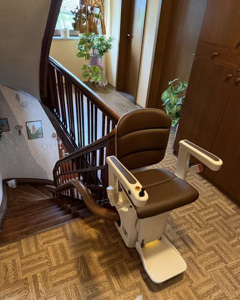 Projekte Detailaufnahme des modernen Kurventreppenlifts mit braunem Sitz am oberen Ende der historischen Holztreppe in Uffenheim.