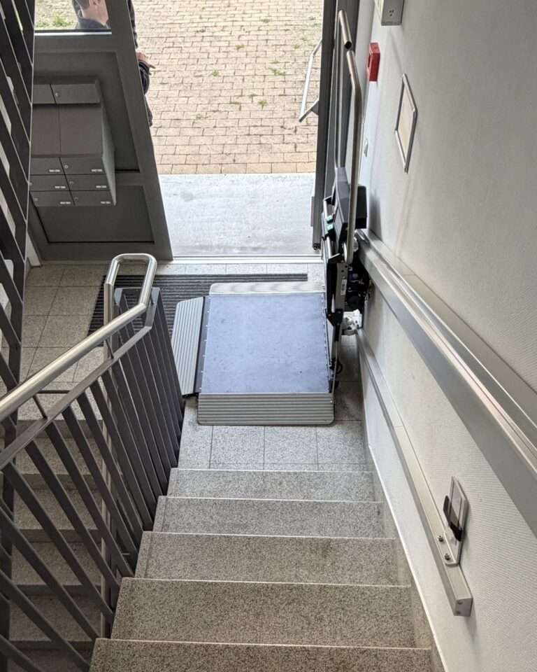 Projekte Blick das Treppenhaus hinab auf den Plattformlift, der sich direkt neben der Eingangstür in der Parkposition befindet.