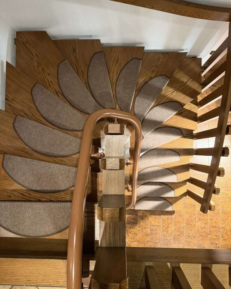 Projekte Symmetrische Draufsicht auf die Kurve der Holztreppe mit der passgenau installierten, braunen Treppenliftschiene von Paitsch Lifte.