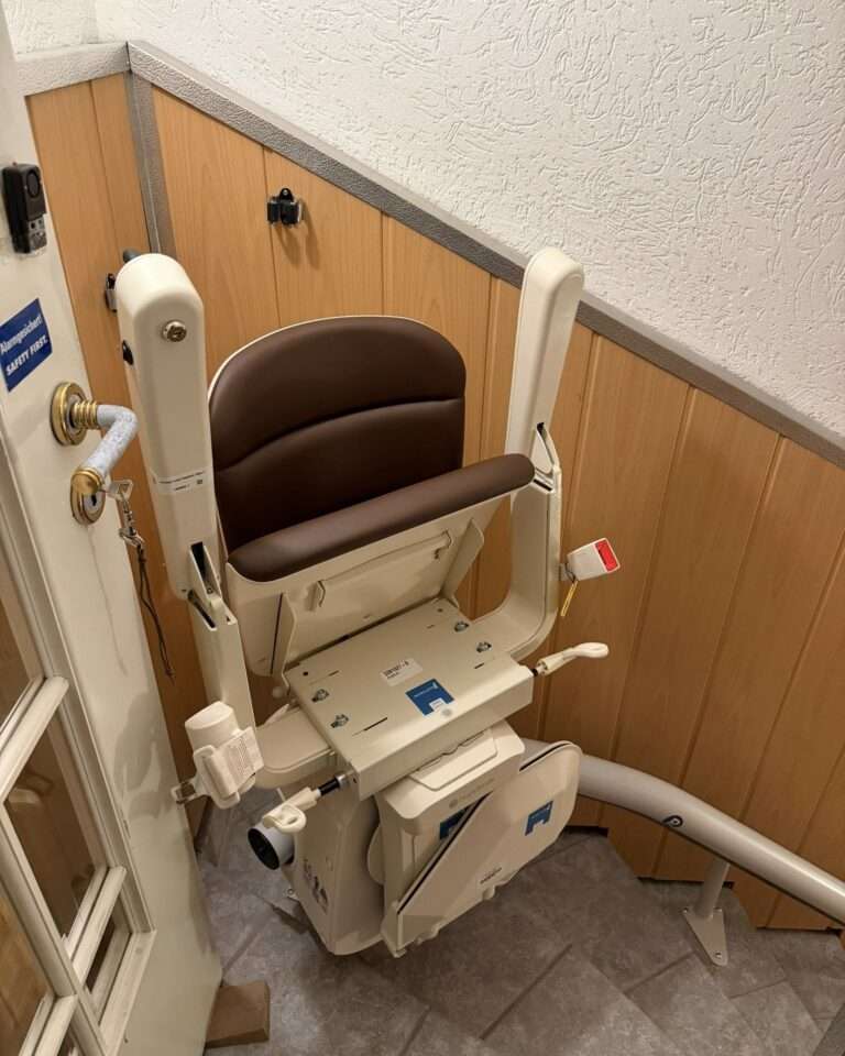 Projekte Platzsparend zusammengeklappter Treppenlift in der zusätzlichen Parkposition, damit sich die obere Tür frei öffnen und schließen lässt.