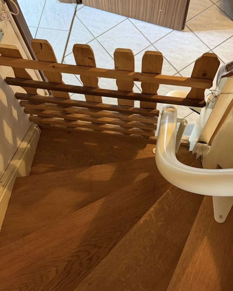 Projekte Blick von oben auf eine geschlossene Haustür-Absperrung aus Holz, die exakt an den Verlauf der weißen Treppenlift-Fahrschiene auf den Holzstufen angepasst wurde.