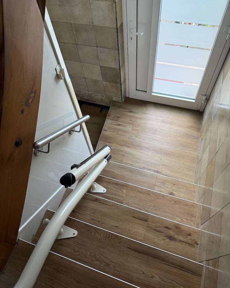 Projekte Blick von oben auf die hochgeklappte Schiene des Treppenlifts im Flur, die den Durchgang und Kellerzugang barrierefrei freigibt.