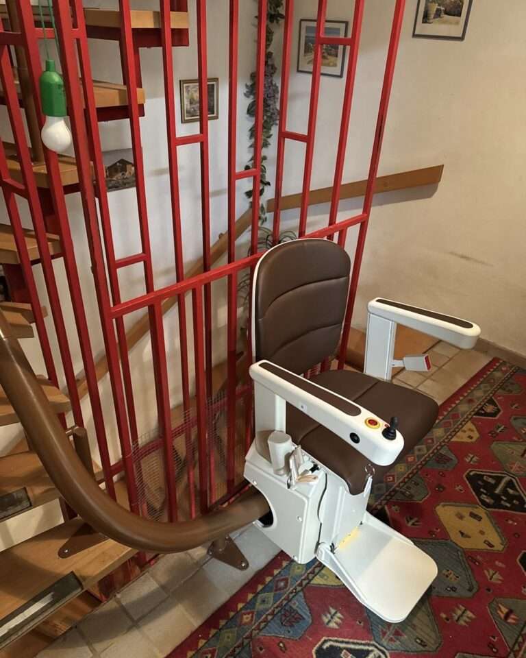 Projekte Kurven-Treppenlift mit braunem Kunstledersitz und platzsparendem Einrohr-Schienensystem an einer Holztreppe in Köfering.