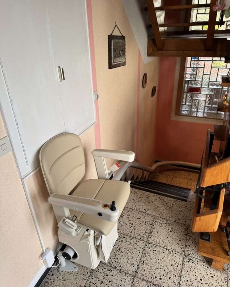 Projekte Platzsparender Kurven-Treppenlift mit beigefarbenem Sitz und unauffälliger Schienenführung entlang der Wand in Mitteleschenbach.