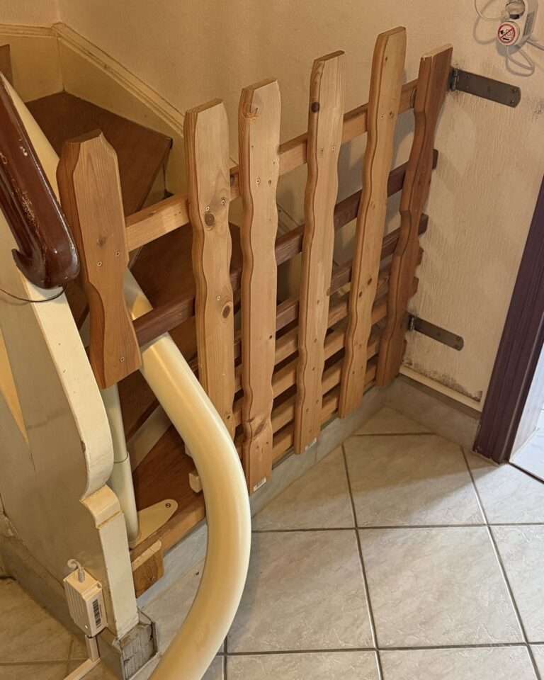 Projekte Detailaufnahme der hölzernen Absperrtür, deren Latten präzise um die weiße Fahrschiene des Treppenlifts herum ausgespart wurden, um volle Funktion zu gewährleisten.