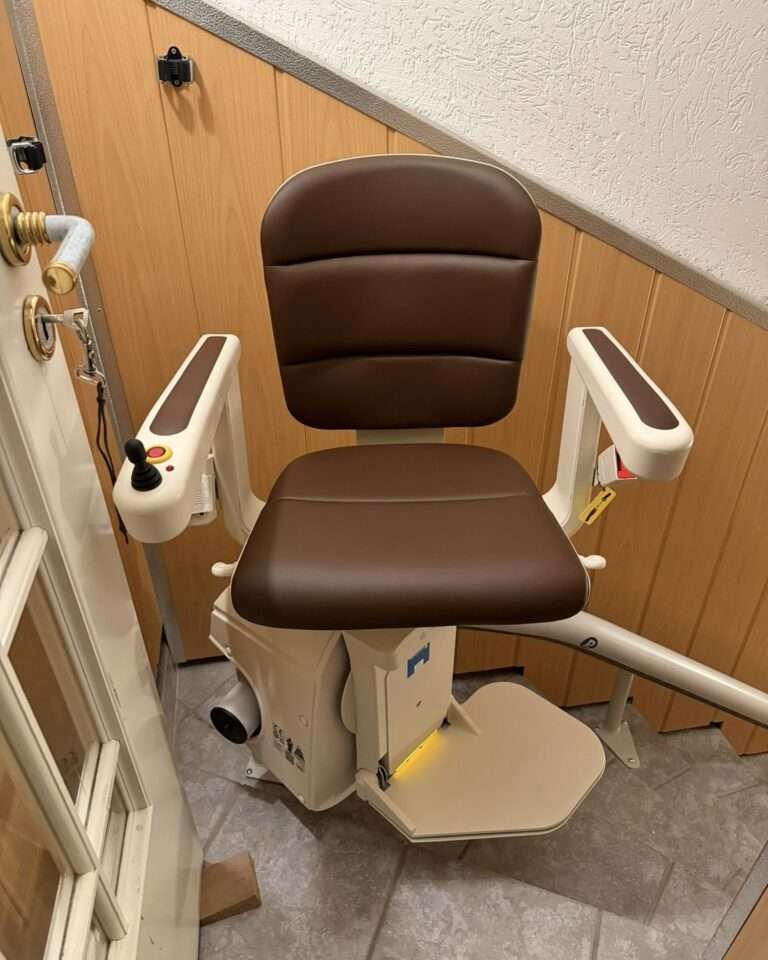 Projekte Kurventreppenlift mit braunem Polstersitz in der oberen Etage fahrbereit direkt neben einer nach innen öffnenden Tür.
