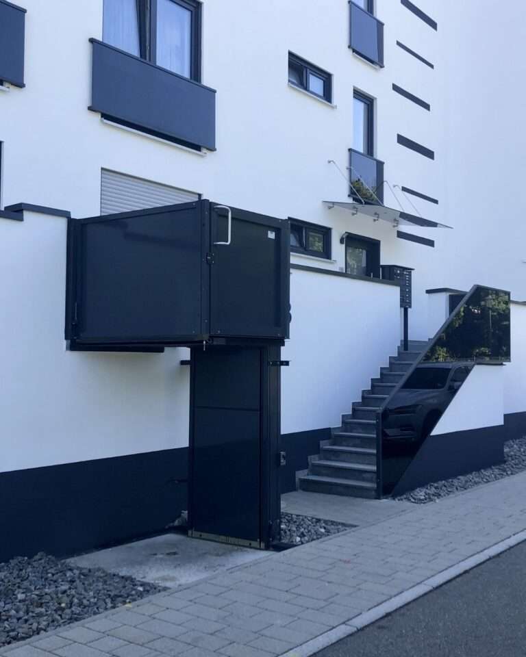 Schwarzer Hublift im Außenbereich neben einer Außentreppe als barrierefreier Zugang zum Hauseingang