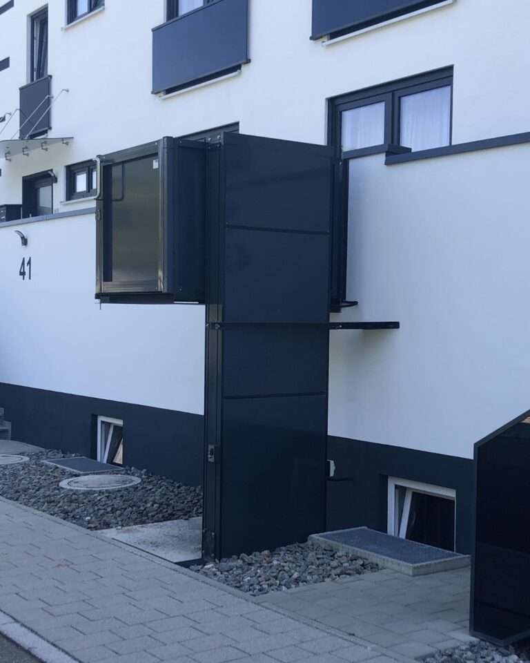 Moderner schwarzer Hublift in angehobener Position an der Außenfassade eines Wohngebäudes