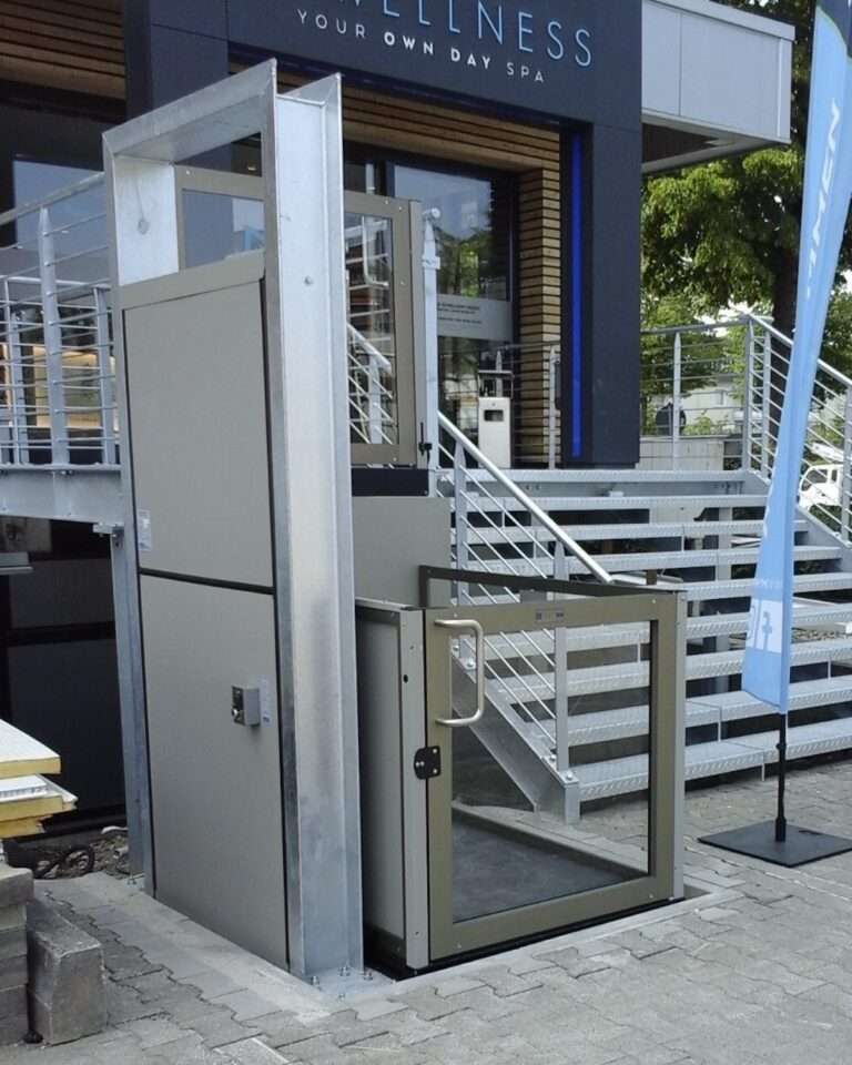 Moderner Hublift mit Glas-Sicherheitstür vor einem Geschäftsgebäude als barrierefreier Zugang