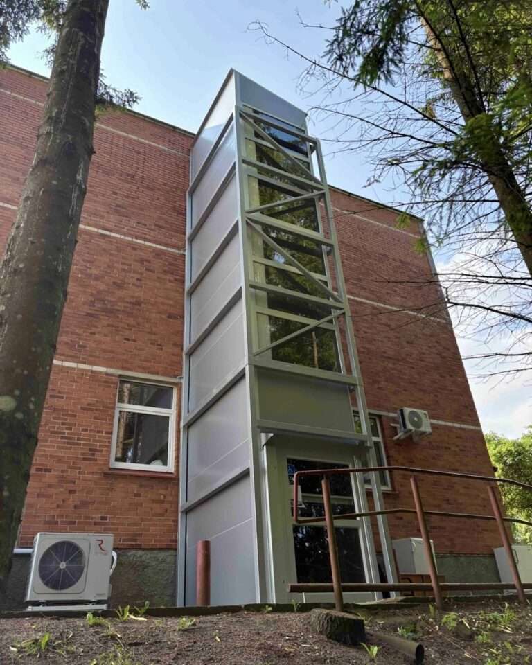 Moderner Außenaufzug im Glasschacht an der Klinkerfassade eines mehrstöckigen Gebäudes